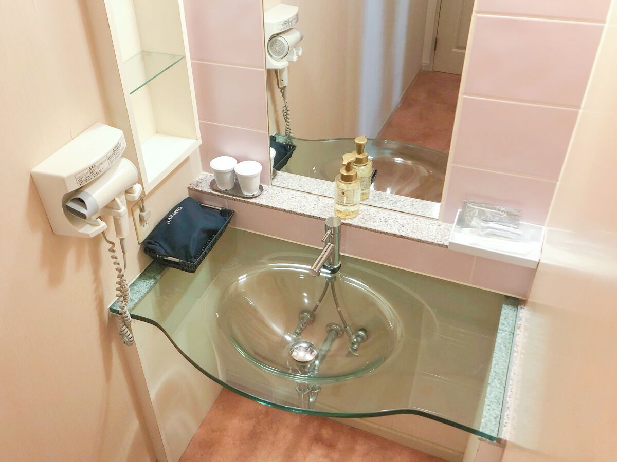 Ett badrum med en handfat av glas, en hårtork och hygienartiklar på hyllan.