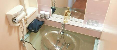 A bathroom with a glass sink, a hairdryer, and toiletries on the counter.