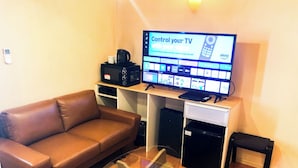 Ein Wohnzimmer mit einer braunen Ledersofa, einem Glastisch, einem Flachbildfernseher, einer Stereoanlage und einem kleinen schwarzen Tisch.