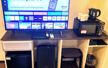 A television with a remote control, a coffee maker, and a microwave on a desk.