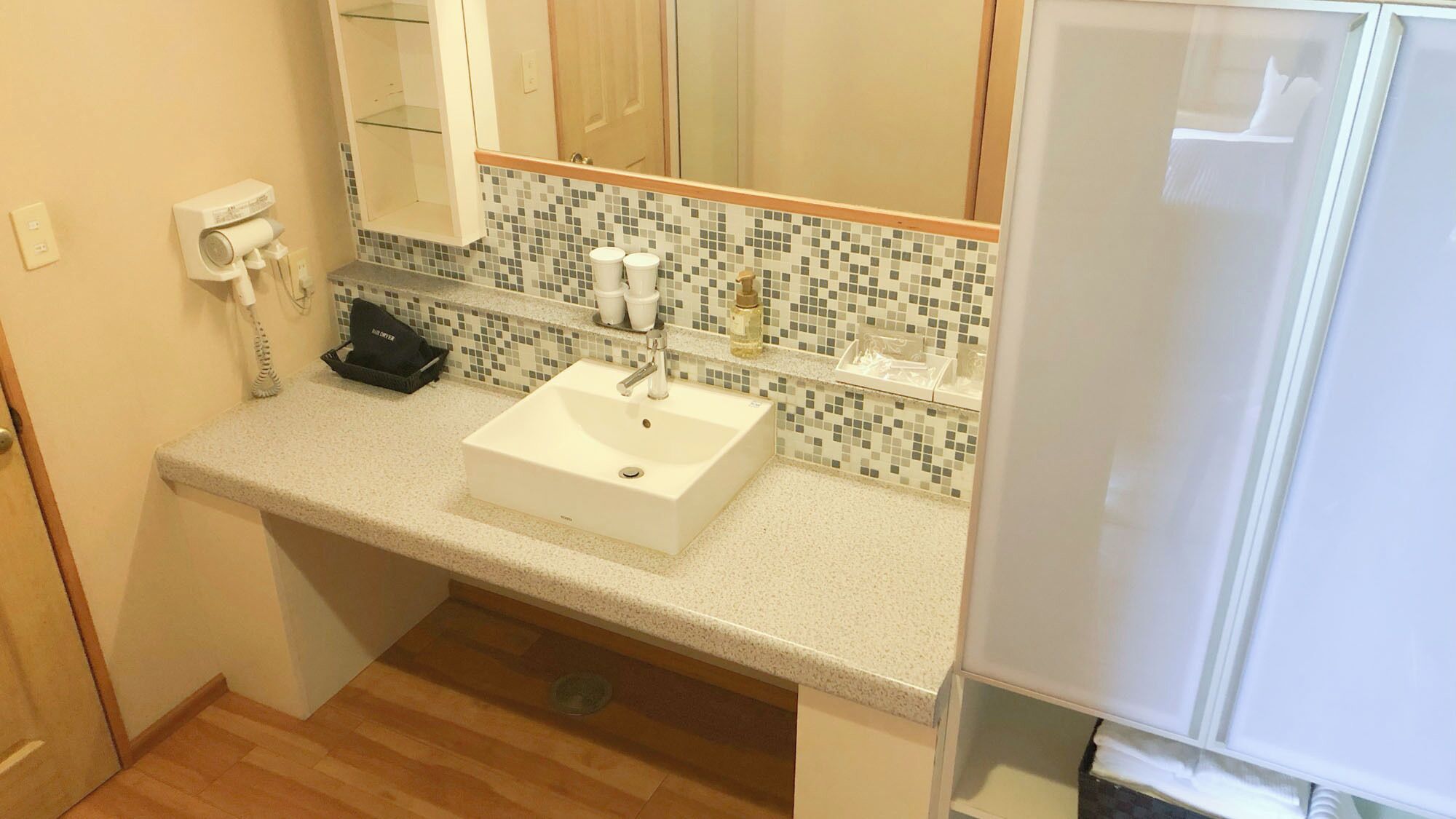 Un baño con un lavabo blanco, un espejo, salpicadero de azulejos y suelo de madera.