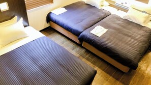 A hotel room with two single beds, each with a pillow and a folded towel. The room has wooden flooring and a window with blinds. - HOTEL LiVEMAX Kuroishi (Kuroishi)