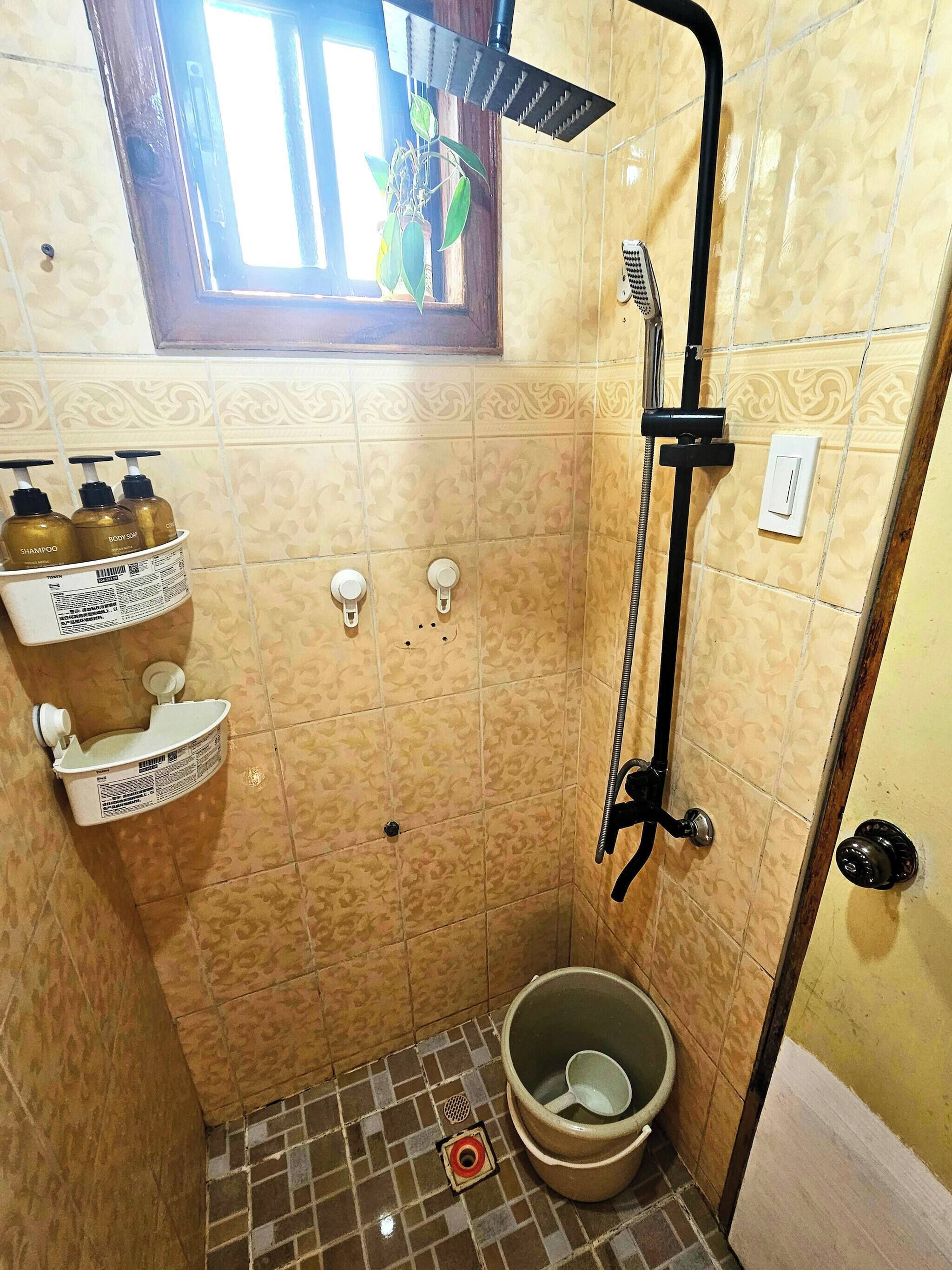 A small, tiled bathroom with a shower, a toilet, and a shelf with toiletries.