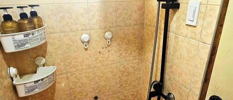 A small, tiled bathroom with a shower, a toilet, and a shelf with toiletries.