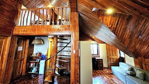 Un interior rústico de madera con un entrepiso, una escalera y una sala de estar con sofá.