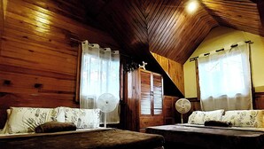 Acogedora habitación tipo cabaña con paredes de madera, dos camas con ropa de cama floral, un armario de madera y un ventilador de techo.