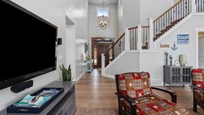 A spacious living room with a large flat-screen TV, a comfortable seating area with patterned cushions, and a staircase leading to an upper level.