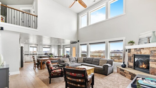 A spacious living room with a fireplace, large windows, and a kitchen in the background.