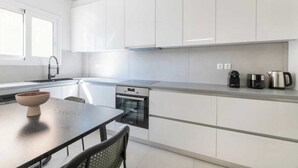 A modern kitchen with white cabinets, a black countertop, a built-in oven, and a dining area with a table and chairs. - Modern Athenian Nest near Kallimarmaro Stadium (Athina)