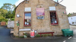 A stone building with signs for a community shop, a church, and a terrace. - The Museum (Alston)