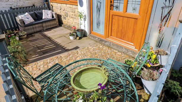 A cozy outdoor seating area with a stone patio, a metal table, and a small garden. - The Museum (Alston)