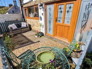 A cozy outdoor seating area with a stone patio, a metal table, and a small garden. - The Museum (Alston)
