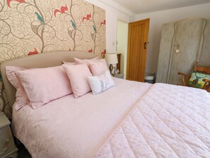 Un dormitorio con cama, almohadas, mesita de noche, lámpara, armario y una silla.