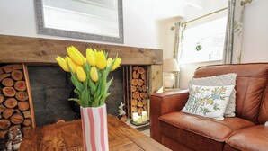 A living room with a wooden coffee table, a brown leather sofa, a striped vase with yellow flowers, a fireplace, and a window with curtains. - The Museum (Alston)