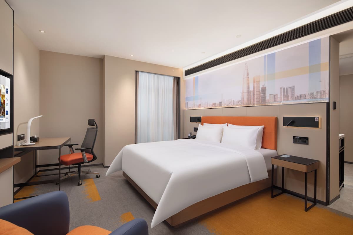 Una habitación de hotel moderna con una cama grande, un escritorio, una silla y vistas a un horizonte urbano.