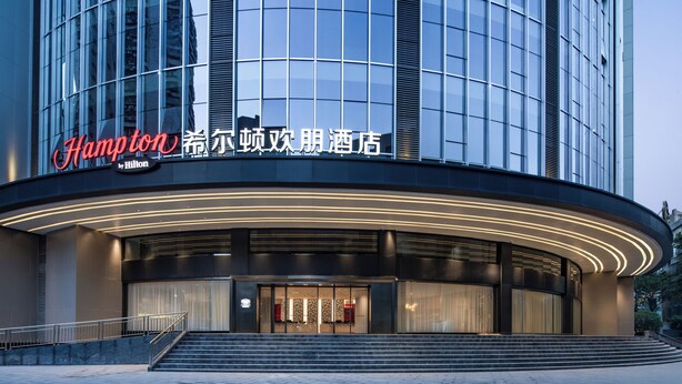 Un hotel moderno con un ingresso curvo, illuminato da luci soffuse, e il logo Hilton ben visibile.