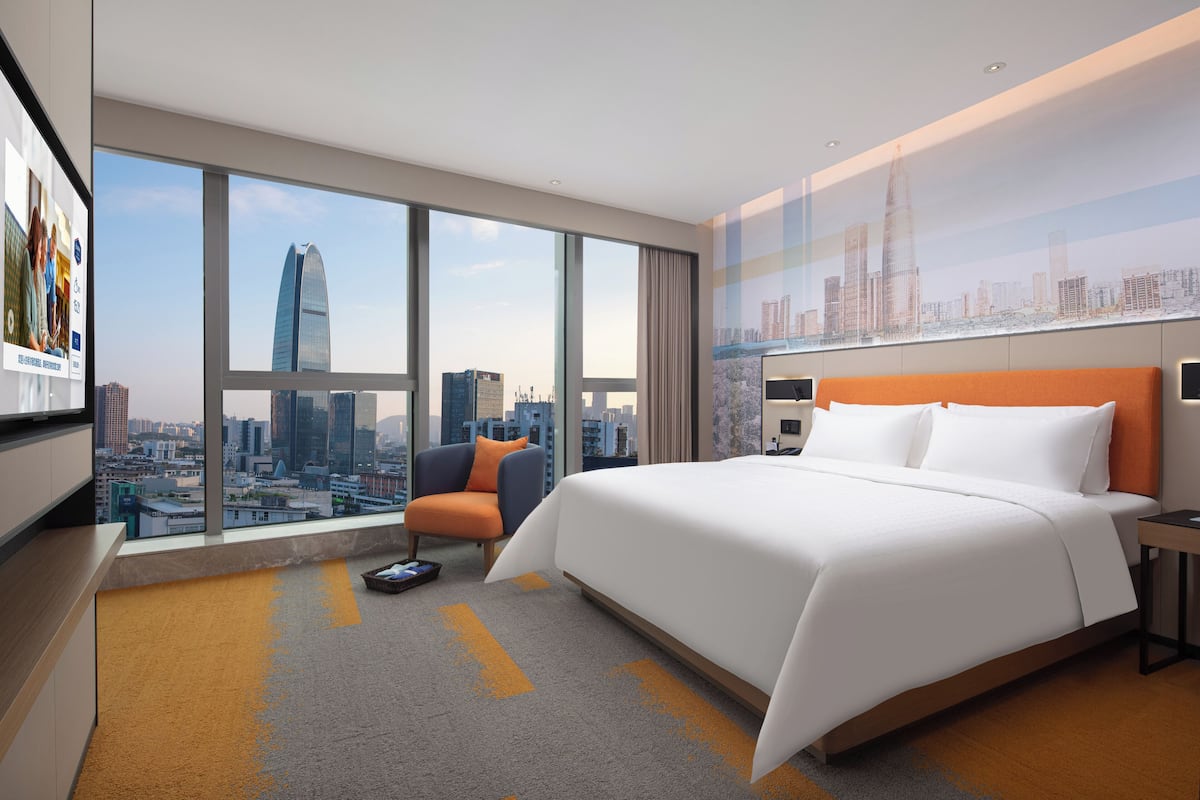 Una habitación de hotel moderna con una cama grande, una silla, un escritorio y vistas a la ciudad.
