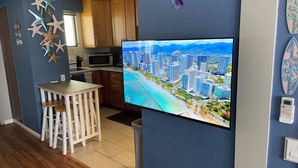 A modern kitchen with wooden cabinets, a microwave, and a dining area with a white table and chairs. - Adorable 1-bedroom condo with kitchen, pool, WiFi near Waikiki Beach, sleeps 6-8 (Honolulu)