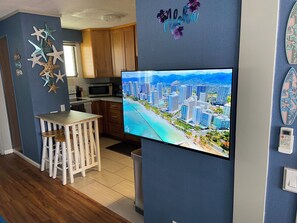A modern kitchen with wooden cabinets, a microwave, and a dining area with a white table and chairs. - Adorable 1-bedroom condo with kitchen, pool, WiFi near Waikiki Beach, sleeps 6-8 (Honolulu)