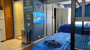 A bedroom with a bunk bed, a small trash bin, a refrigerator, and a cityscape painting on the wall. - Adorable 1-bedroom condo with kitchen, pool, WiFi near Waikiki Beach, sleeps 6-8 (Honolulu)