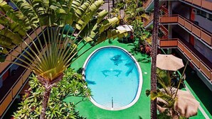 A rooftop pool surrounded by lush greenery and a multi-story building with balconies. - Adorable 1-bedroom condo with kitchen, pool, WiFi near Waikiki Beach, sleeps 6-8 (Honolulu)