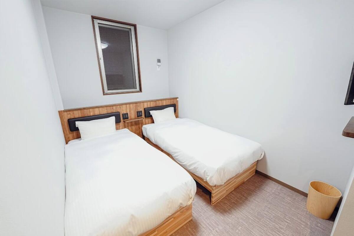 Una habitación pequeña y limpia con dos camas individuales, cabecero de madera, una ventana y piso de madera.