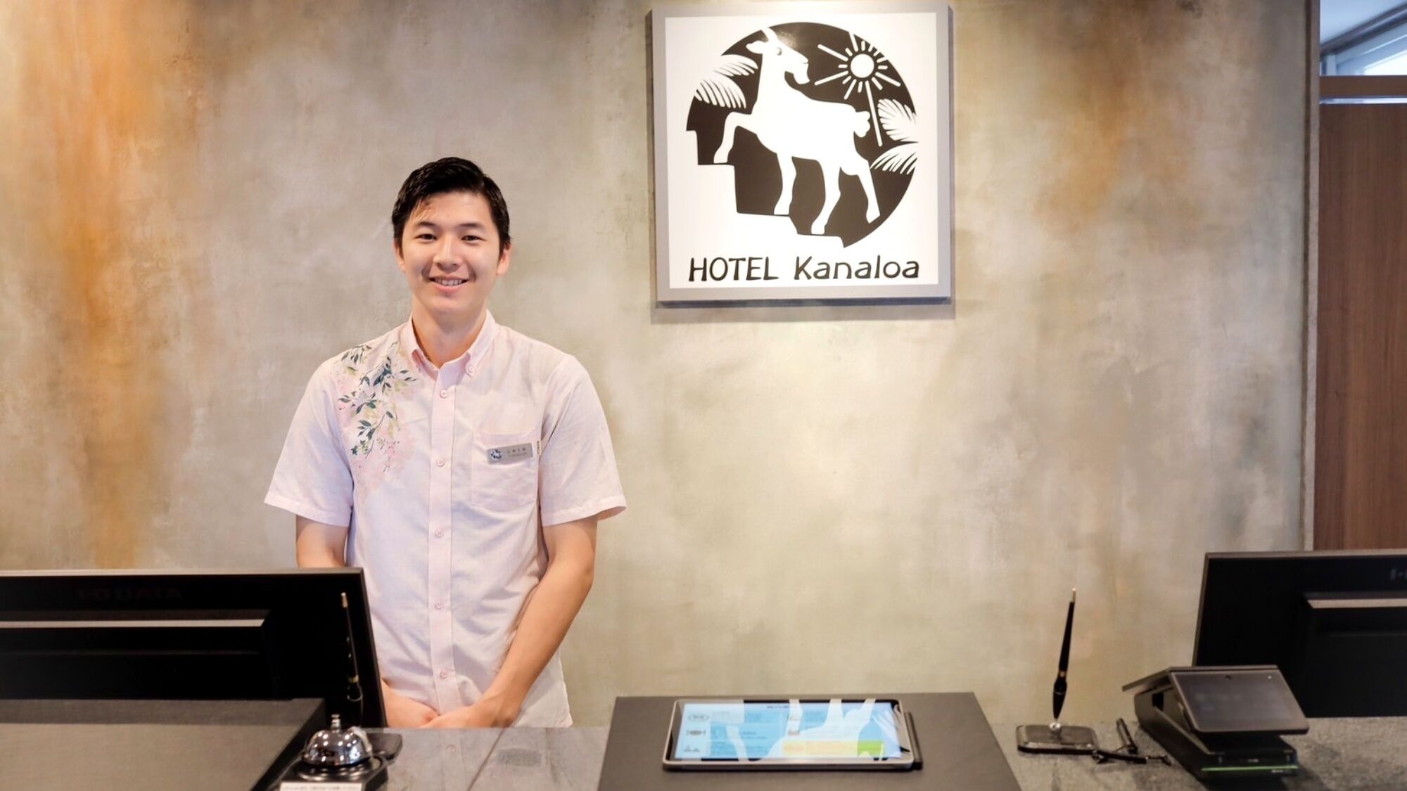 A hotel reception desk with a digital tablet, a traditional bell, and a smartphone charging station.