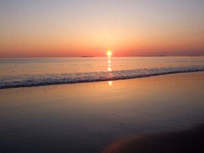 A beach at sunset with calm waves and a clear sky.