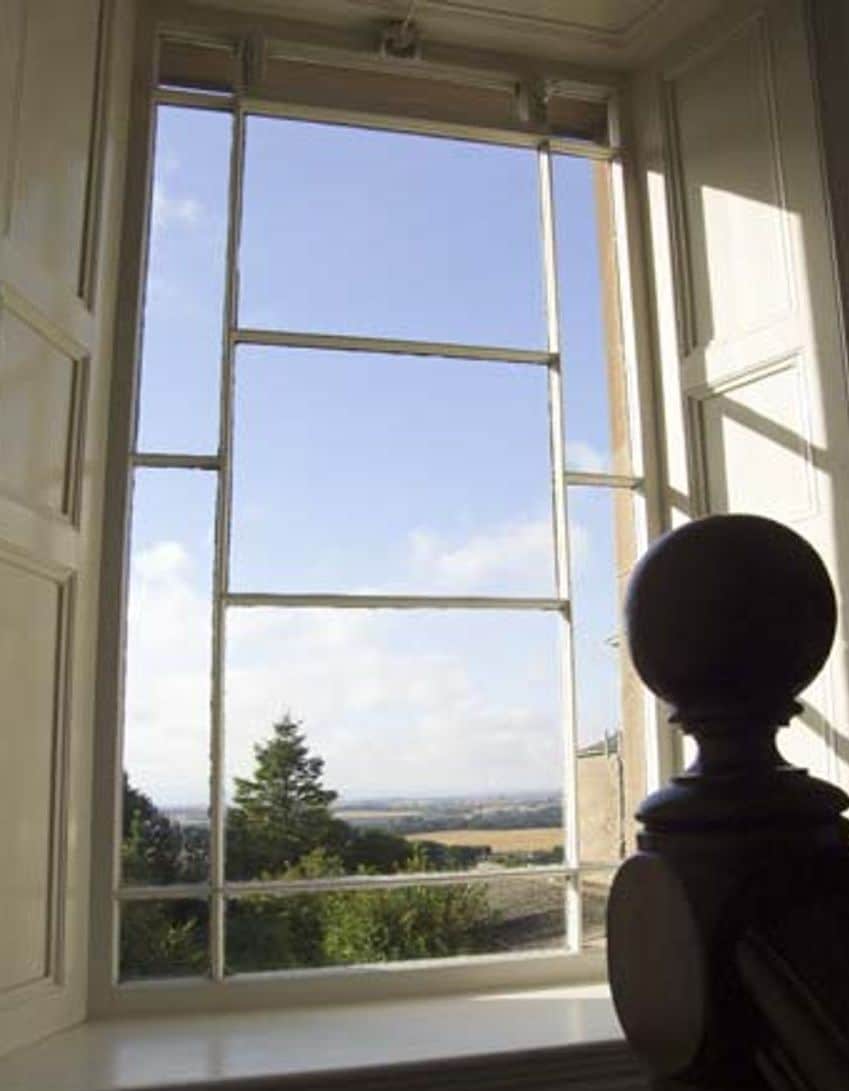 A window with a view of a landscape, a balustrade, and a door frame.