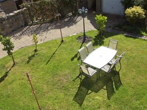 A patio with a white table and four chairs, surrounded by a well-maintained lawn and a stone pathway.