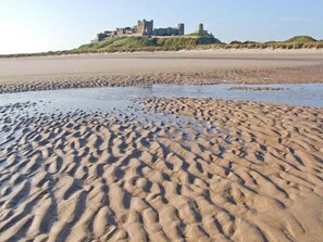 A sandy beach with footprints leading to a castle on a hill. - Bank View (Duns)