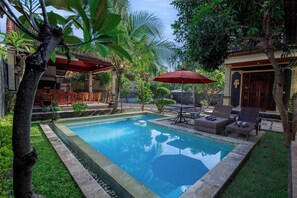 A swimming pool surrounded by lush greenery, outdoor furniture, and a covered seating area. - Sekarinis Place Amed  (Karangasem)