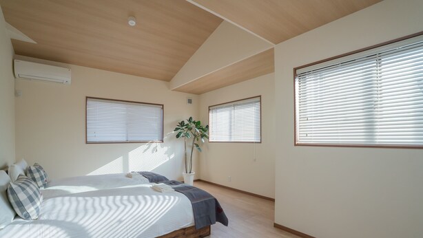 Quarto com cama, planta em vaso e janelas grandes.