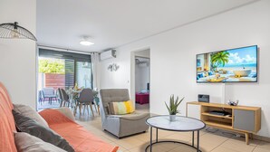 Un salon moderne avec un canapé, un fauteuil et une table basse ronde. Un téléviseur est fixé au mur, et un meuble en bois se trouve en dessous.