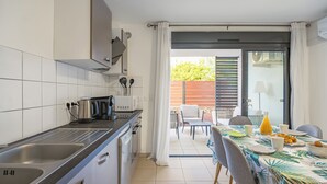 Une cuisine moderne équipée d’un évier, d’une cuisinière et d’un four à micro-ondes. On y trouve également un coin repas avec une table dressée pour deux personnes, agrémentée d’une nappe aux motifs tropicaux.