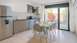 Une cuisine moderne équipée d’appareils électroménagers en acier inoxydable, un coin repas avec une table pour quatre personnes et une porte-fenêtre coulissante donnant sur une terrasse extérieure.