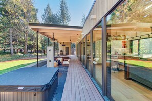 Una terraza moderna al aire libre con jacuzzi, zona de estar y paredes de vidrio que ofrecen vistas al bosque circundante.