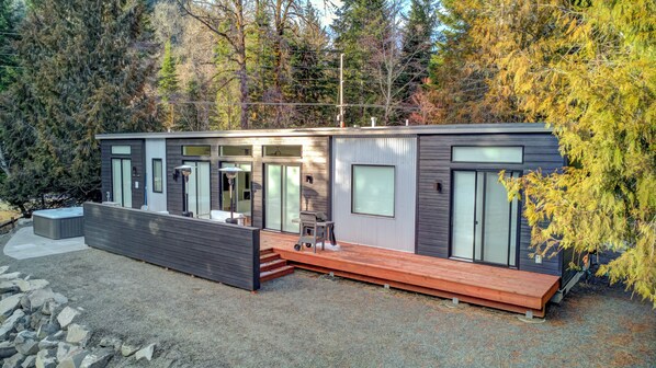 A modern cabin with a deck, large windows, and a hot tub.