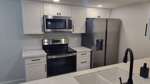 A modern kitchen with white cabinetry, a stainless steel refrigerator, a microwave, an oven, and a sink with a black faucet. - Cozy 1-bedroom condo resort in charming Mesa with WiFi, AC (Mesa)