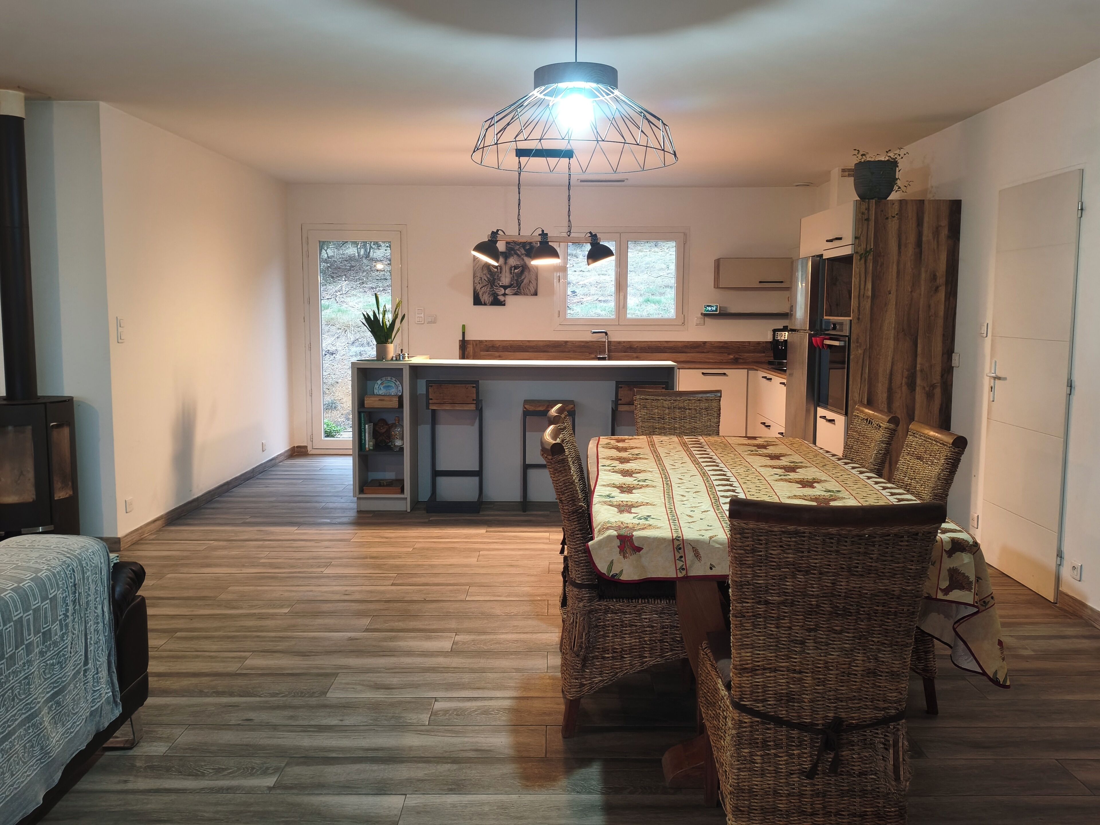 Amplia sala de estar con una mesa de comedor, sillas de mimbre, una isla central con fregadero y una lámpara colgante moderna.