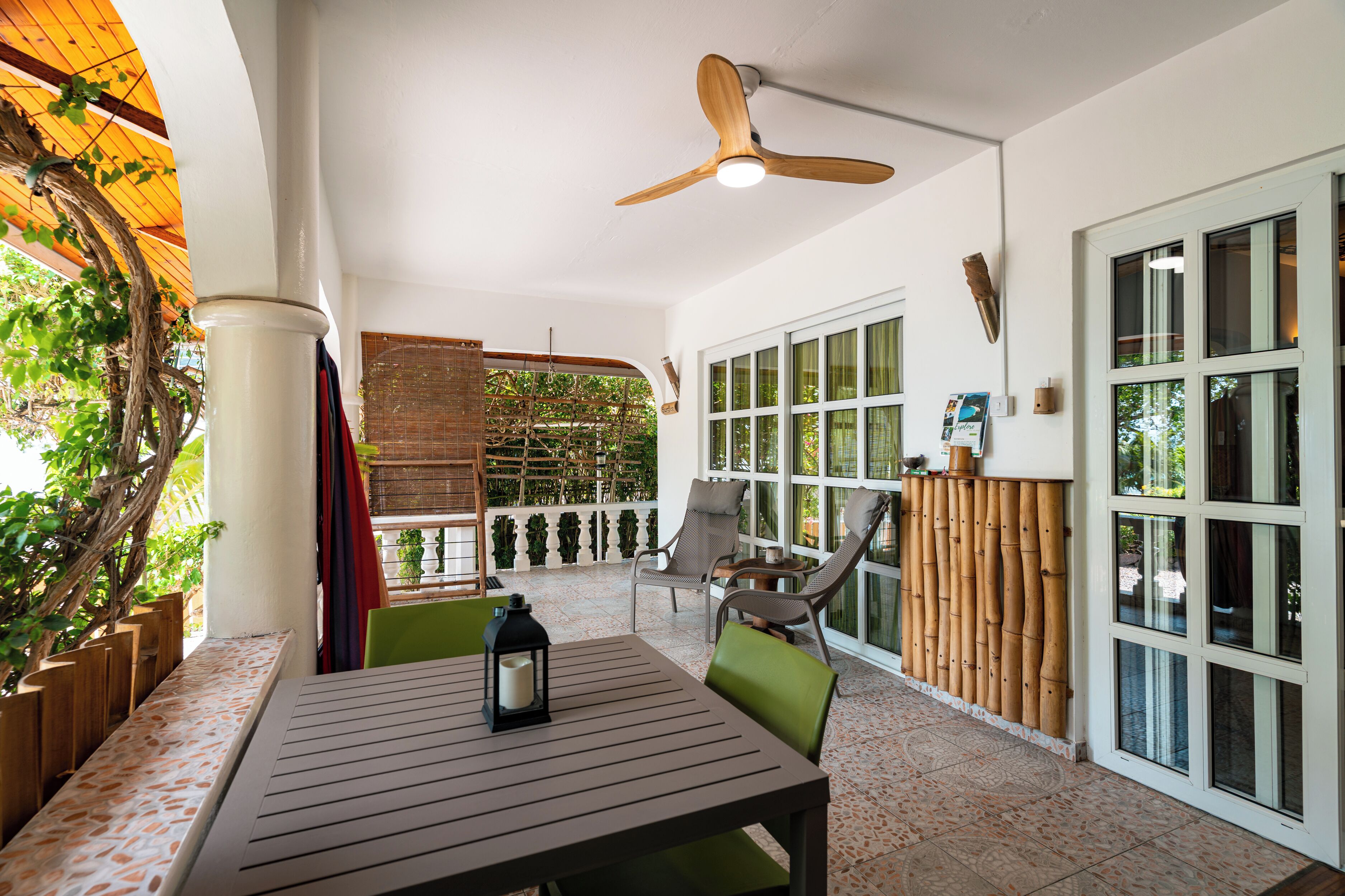 Un patio techado con mesa y sillas, un ventilador de techo y vistas a zonas verdes.