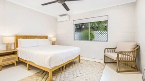 Ein Schlafzimmer mit einem Bett, einem Sessel, einem Deckenventilator, einem Fenster und einem Nachttisch.