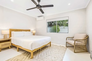 A bedroom with a bed, a chair, a ceiling fan, a window, and a nightstand.