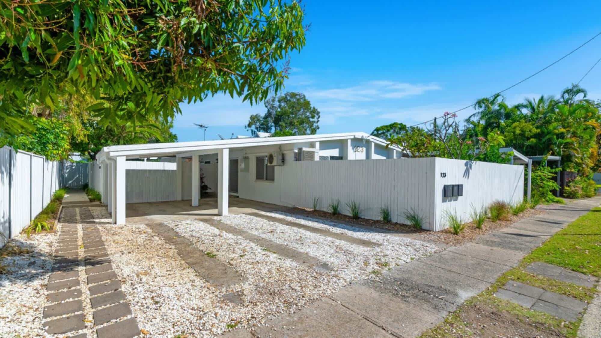 A single-story building with a covered patio area, a gravel driveway, and a white fence surrounding the property.