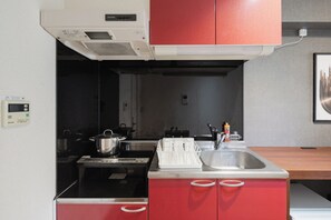 A compact kitchen with a stove, sink, and red cabinets. - HIT Tenjin (Fukuoka)