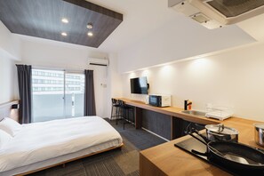 Habitación de hotel con cama, kitchenette, televisor y ventana con cortinas.