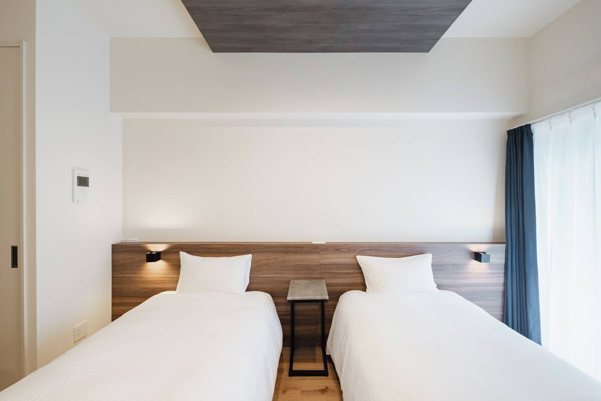 A hotel room with two beds, a small table, and a nightstand with a lamp.