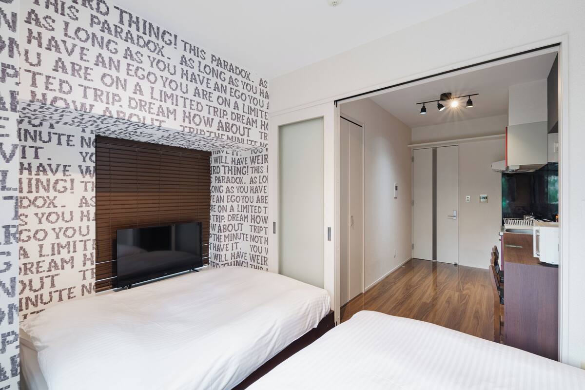 A modern hotel room with a bed, a TV, and a wall with motivational text.