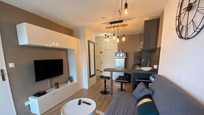 A modern living room with a flat-screen TV, a round coffee table, and a grey sofa with teal cushions.