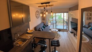 A modern kitchen with a built-in oven, a dining area with a bench and stools, a large window with a view of the city, and a living area with a sofa and a TV.